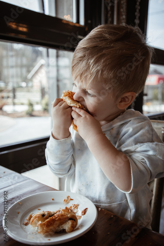 Toddler boy at a cafe biting into croissant at a coffee shop
