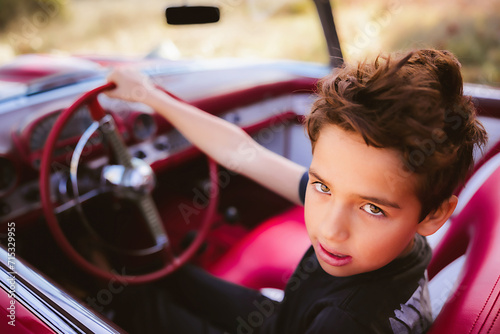 Young boy sitting in red classic car pretending driving photo