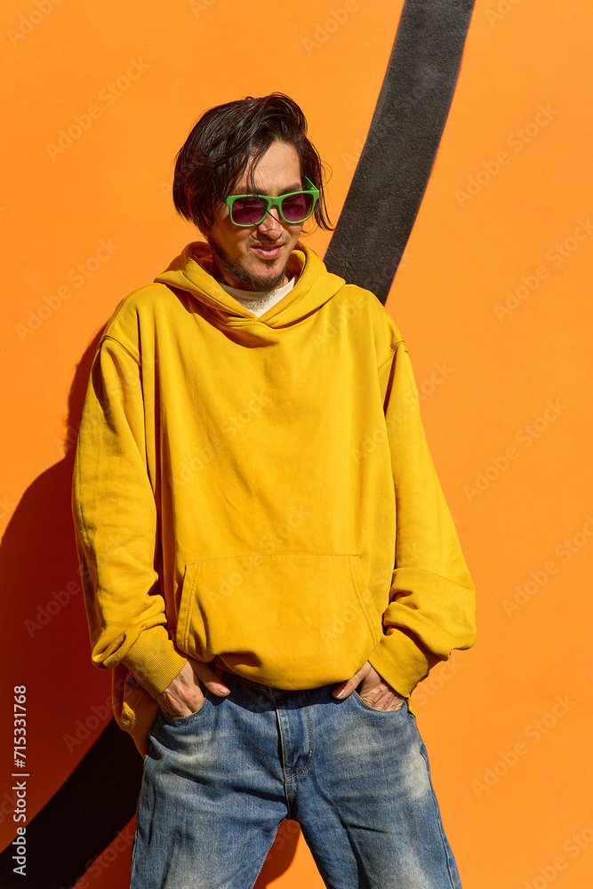An Asian guy in stylish green glasses stands against a yellow wa An Asian guy in stylish green glasses stands against a yellow wa