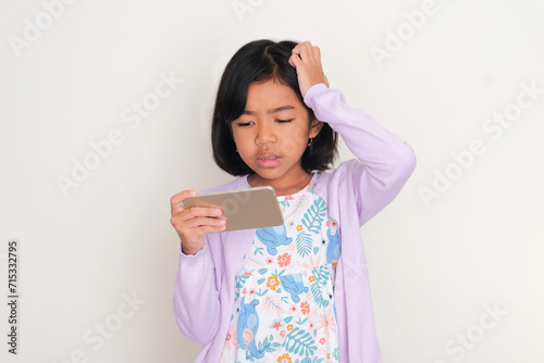 Asian kid looking to mobile phone that she hold with confused expression photo