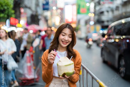 Young asian woman traveller standing and drinking coconut water. Beauty traveller female in city lifestyle chinatown street food market Bangkok, Thailand photo
