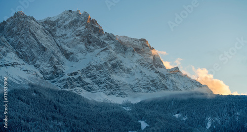 A bottom up view to the ice cold and with snow covered Zugspitze mountain chain and the surrounding forest nature landscape