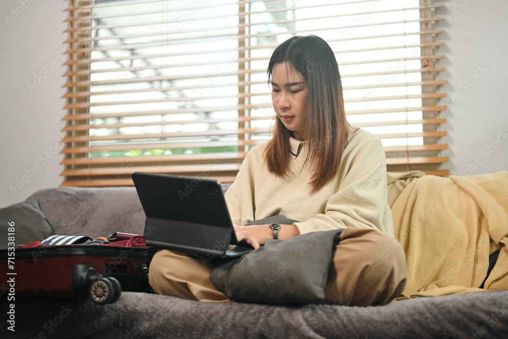 Smiling young woman using laptop for choosing travel destination for trip or booking hotel online Smiling young woman using laptop for choosing travel destination for trip or booking hotel online