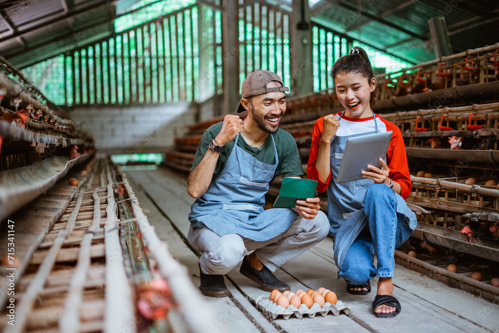 Obraz premium happy entrepreneur couple see income in savings book and tablet during egg harvest squat at poultry farm