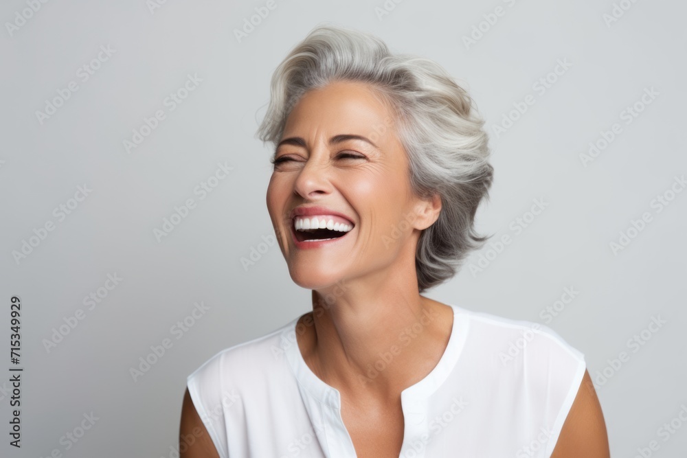 Portrait of beautiful senior woman laughing and looking at camera on grey background Portrait of beautiful senior woman laughing and looking at camera on grey background