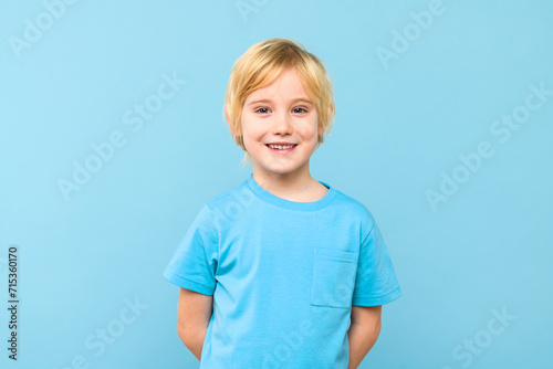 Happy young caucasian preschooler boy in casual outfit smiling, looking at camera, isolated over pastel blue background.