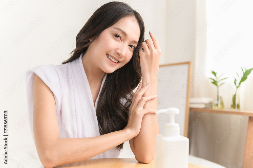 Young beautiful Asian woman applying skin care cream lotion on her arm. Woman beauty selfcare cosmetic caring routine concept.