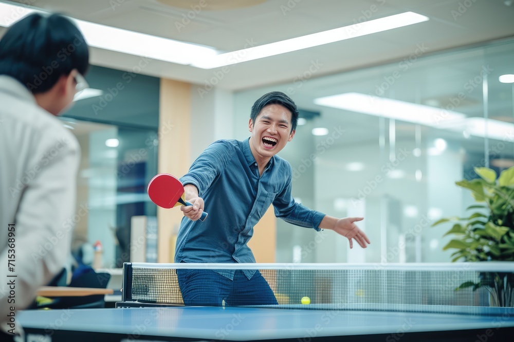 Happy young asian man having fun playing table tennis with colleague in an office zone.