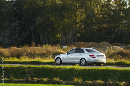 A German luxury car drives along a scenic route with the golden hues of sunset illuminating the tranquil forest.