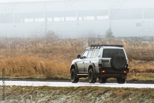 off-road capable SUV truck with offroad tires, big wheels and a 5th wheel on the back travels on an asphalt road with a breathtaking landscape of a golden sunset sky.