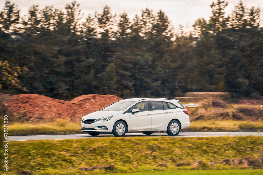 Driving a modern and safe car in the golden hour of dusk. A scenic landscape of forest and road awaits the adventurous travelers. Hybrid vehicle on the road. PZEV in action.
