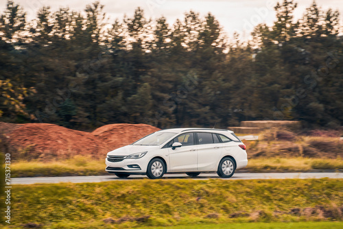 Driving a modern and safe car in the golden hour of dusk. A scenic landscape of forest and road awaits the adventurous travelers. Hybrid vehicle on the road. PZEV in action.