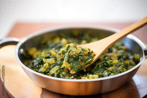 saag aloo being stirred in a pan with a wooden spoon