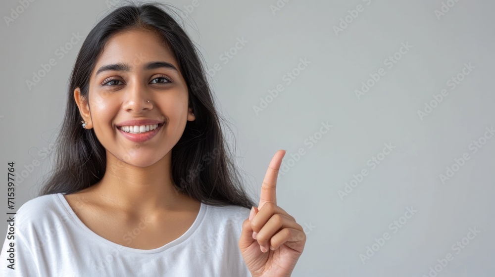 Young Indian woman pointing at gray background with blank space on her hand Happy female student looking at camera advertising product service concept sign Young Indian woman pointing at gray background with blank space on her hand Happy female student looking at camera advertising product service concept sign