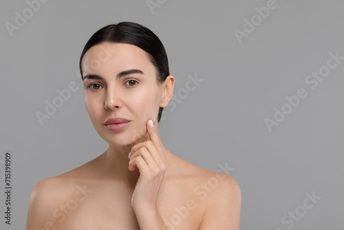 Woman with dry skin checking her face on gray background, space for text