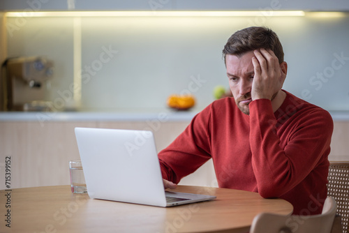 Unhappy man suffering from headache, hangover after party, trying to work on laptop computer, reading document. Exhausted male cant understand, concentrate information because of dizziness, bad memory