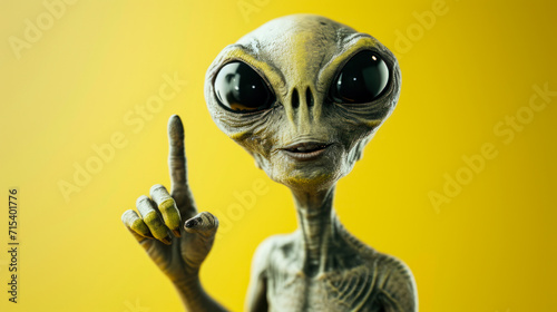 funny portrait of a grey alien pointing up on yellow copy space background