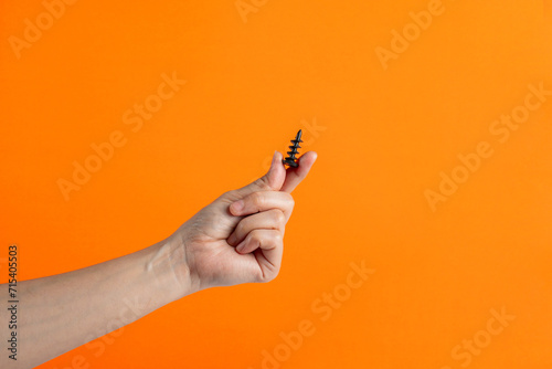 A black screw in hand on orange background. photo