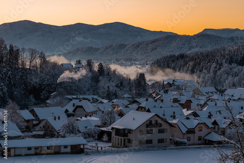 Detail of houses covered with snow in the beautiful village of Ljubno ob Savinji, home of female ski jumping. Early morning with sun just about to rise, yellow skies, white covered forests. photo