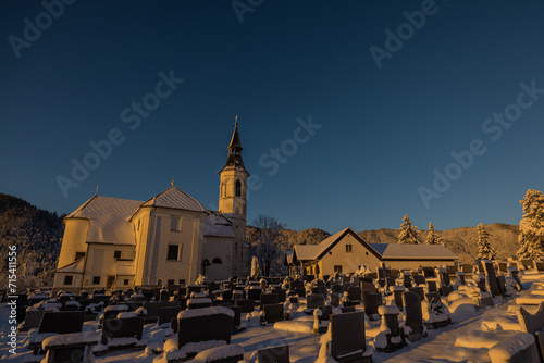 Church of saint mary in the village of Ljubno ob Savinji in early morning during mid-winter, full of snow, graves and church covered with substantial amount of snow. photo