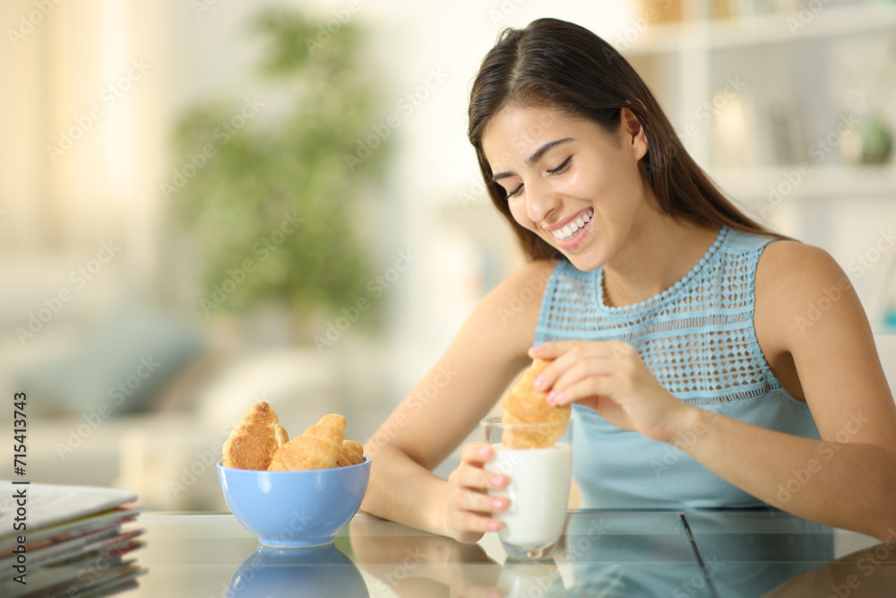 Happy woman eating croissants dipping in milk