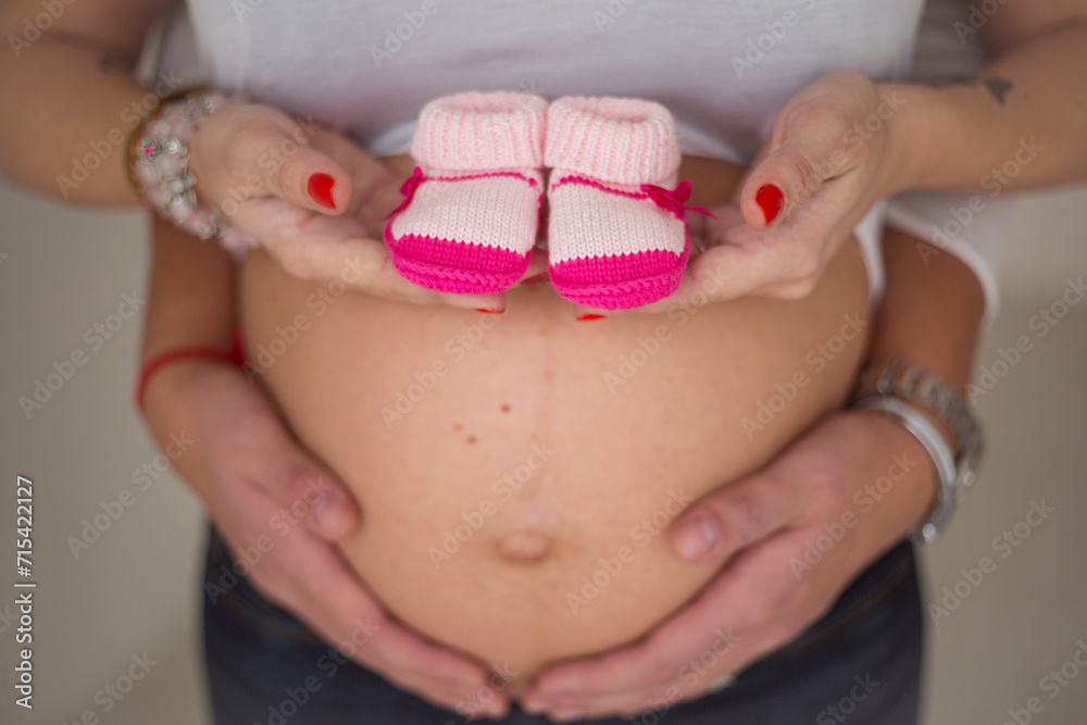 woman with shoes on belly, hands hold booties and pregnant belly woman with shoes on belly, hands hold booties and pregnant belly