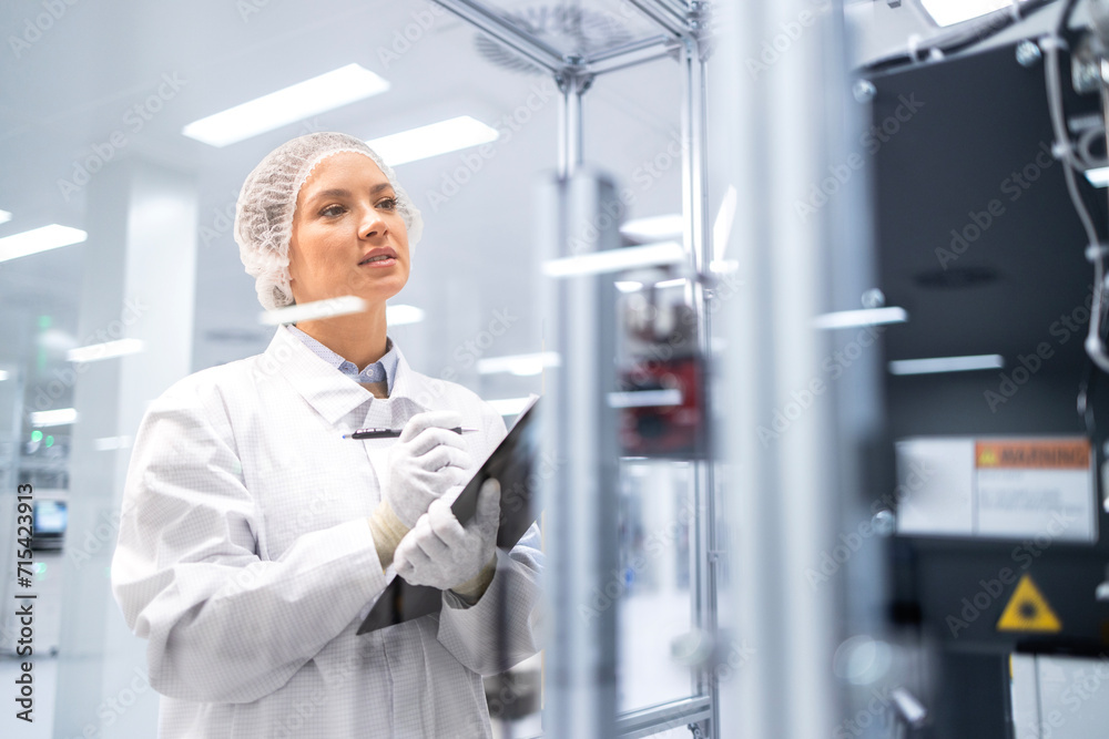 Female factory worker holding checklist and monitoring machine operations in production plant. Female factory worker holding checklist and monitoring machine operations in production plant.