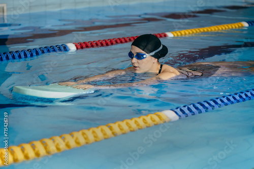 Young woman swims with a board in the pool