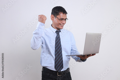 Asian businessman holding a laptop while clenched fist and showing winning expression
