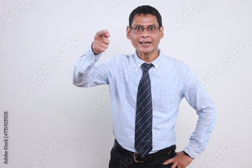 Angry Asian businessman wear glasses shouting and pointing finger at camera isolated over white background