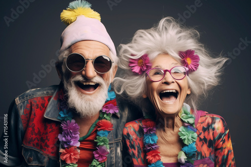 Portrait of crazy and funny couple of old senior man and woman with colorful party clothes. Happy elderly lifestyle concept. Mature man and woman laughing a lot together. Dark background. Happiness