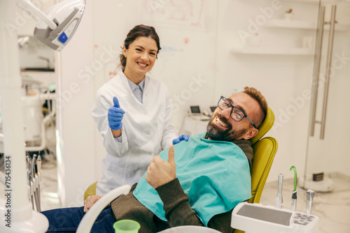 A happy dentist and patient smiling at the camera and giving thumbs up at dentist office.