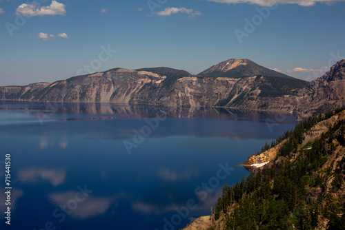 Tranquil Crater Lake, nestled among towering pines, reflects a picturesque snow-capped volcano.