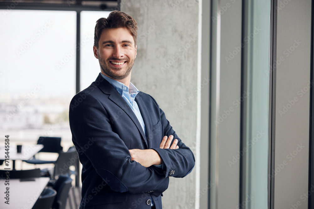 Happy young businessman standing with arms crossed in office Happy young businessman standing with arms crossed in office