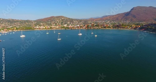 Aerial view of many sailboats anchored in a calm water bay off the coast of a Mexican city tucked into the mountains near Zihuatanejo. photo