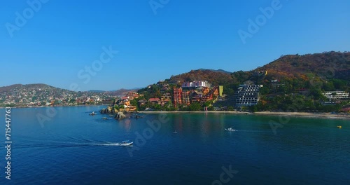 Aerial video flying by the gorgeous shoreline filled with boats, white sand beaches, and the beautiful city of Zihuatanejo, Mexico photo