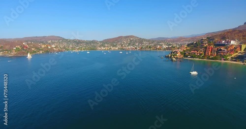 Drone flying high above a still water bay with many boats anchored off the shore of a quiet town on the western coast of Mexico photo