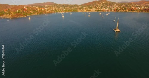Tilting up to reveal a busy ocean bay in Zihuatanejo, Mexico at sunset as the sailboat and yachts return to anchor near shore photo