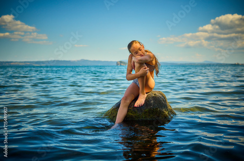 Girl resting on rock in lake Bolsena, Italy