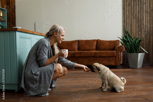Smiling woman feeding snack to Pug dog in living room at home