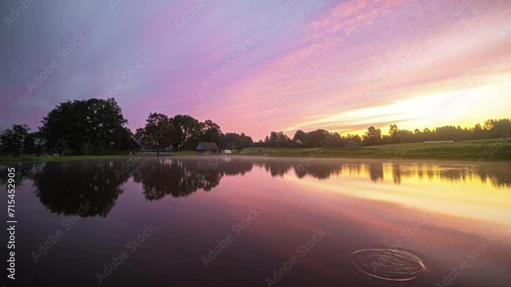 Morning dew and clouds pass over a lake before an orange sunrise announces the day.