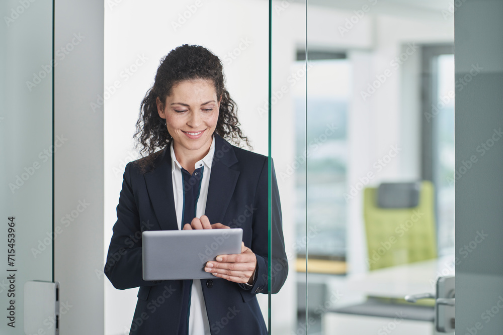 Smiling businesswoman using tablet PC and standing in office doorway Smiling businesswoman using tablet PC and standing in office doorway