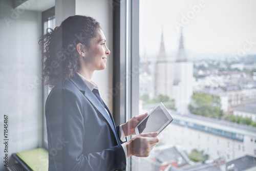 Smiling businesswoman standing with tablet PC near glass window photo