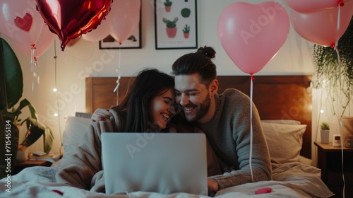 Happy loving couple shopping online while lying in bed and using laptop with heart shape balloons photo