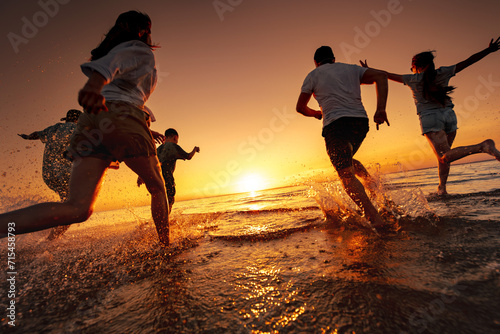 Happy family or company of friends are having fun, runs and jumps and runs at sunset lake beach