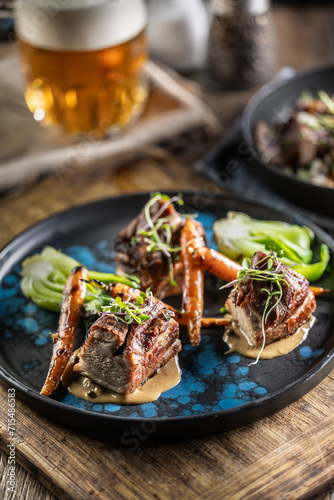 Three pieces of baked belly with grilled vegetables on a plate in a pub or restaurant