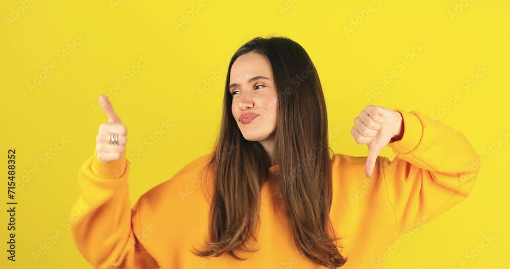 Young woman in yellow hoody making good-bad sign isolated on yellow background. Girl make choice, or makes a decision thumb up or thumb down, like or dislike, yes or no. Young woman in yellow hoody making good-bad sign isolated on yellow background. Girl make choice, or makes a decision thumb up or thumb down, like or dislike, yes or no.