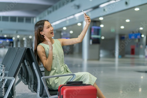 Asian woman with luggage using phone video call while waiting for departure at a transportation departure hall