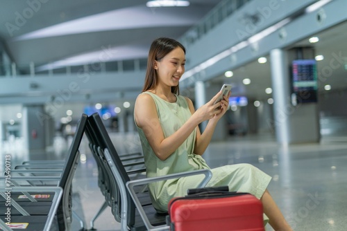 Asian woman with luggage using phone while waiting for departure at a transportation departure hall