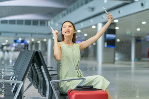 Asian woman with luggage using phone video call while waiting for departure at a transportation departure hall
